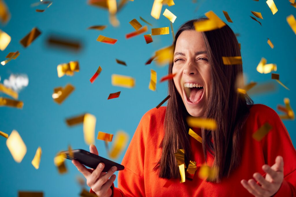 Celebrating Young Woman With Mobile Phone Winning Prizes And Showered With Gold Confetti In Studio