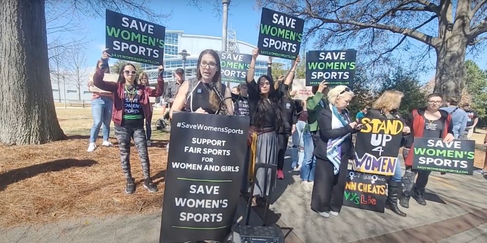 Women's rights protesters holding "save women's sports" signs.