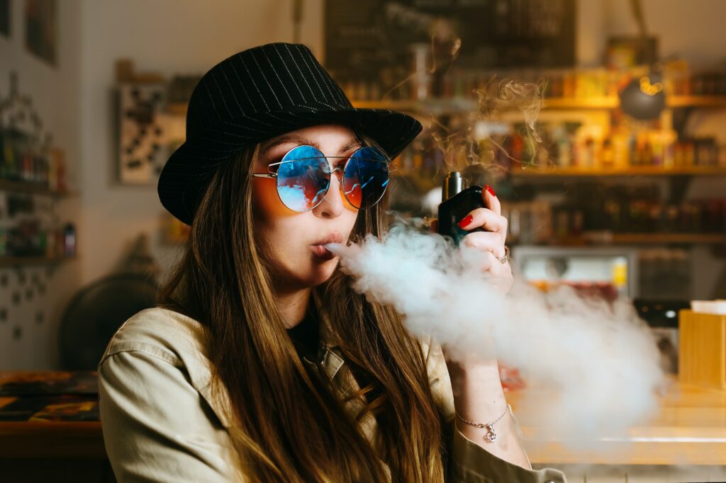 Vaping girl. Young hipster woman vape e-cig at the vapeshop. Hip-hop style. Closeup