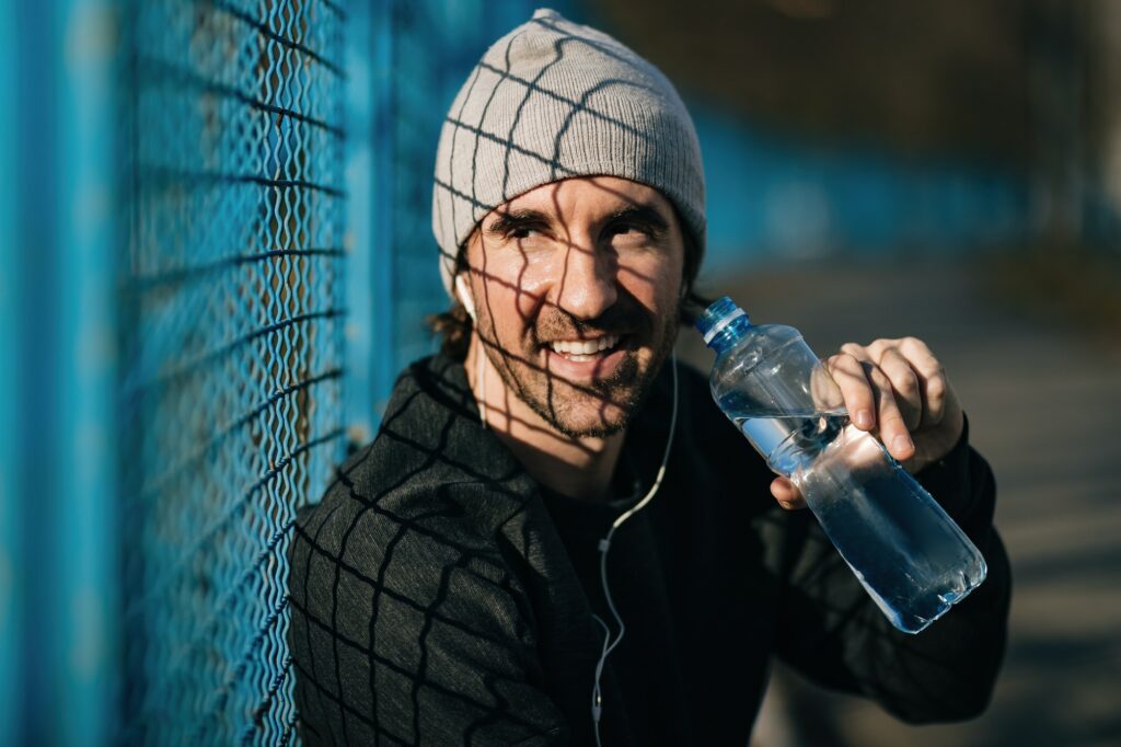 Young happy athlete drinking water while exercising outdoors.