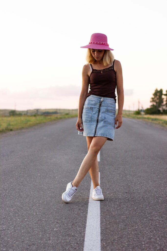 beautiful girl in denim skirt and pink hat stands on the center of the road
