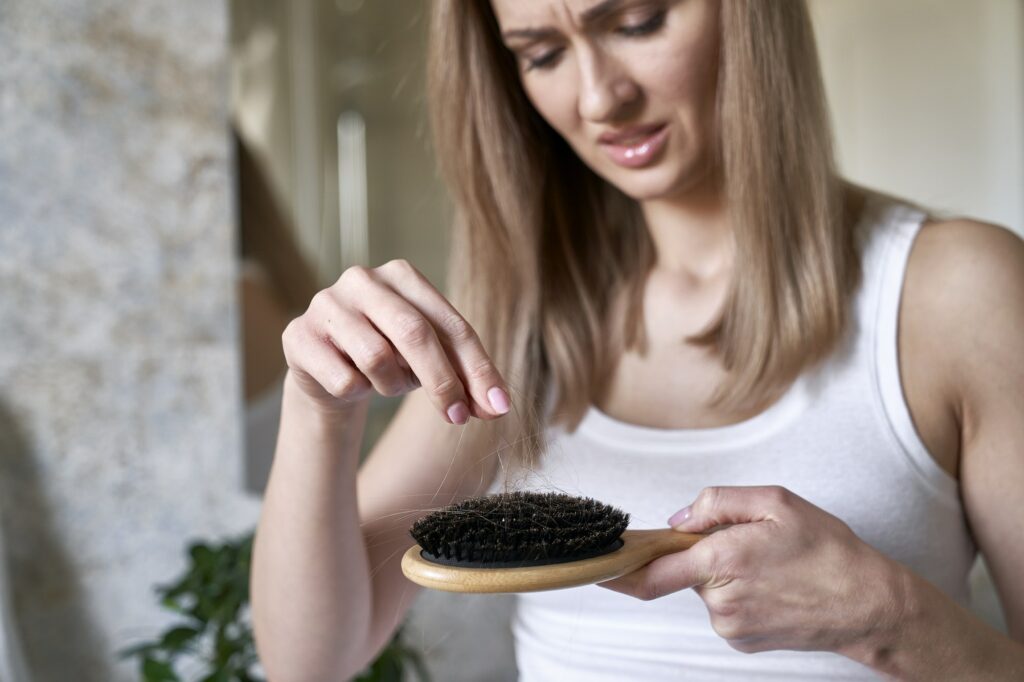 Shocked caucasian woman holding hairbrush with many hair on it