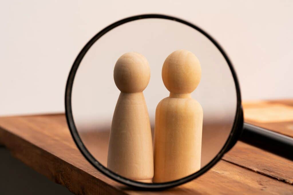 Two wooden figures of people through magnifying glass. Search of love concept
