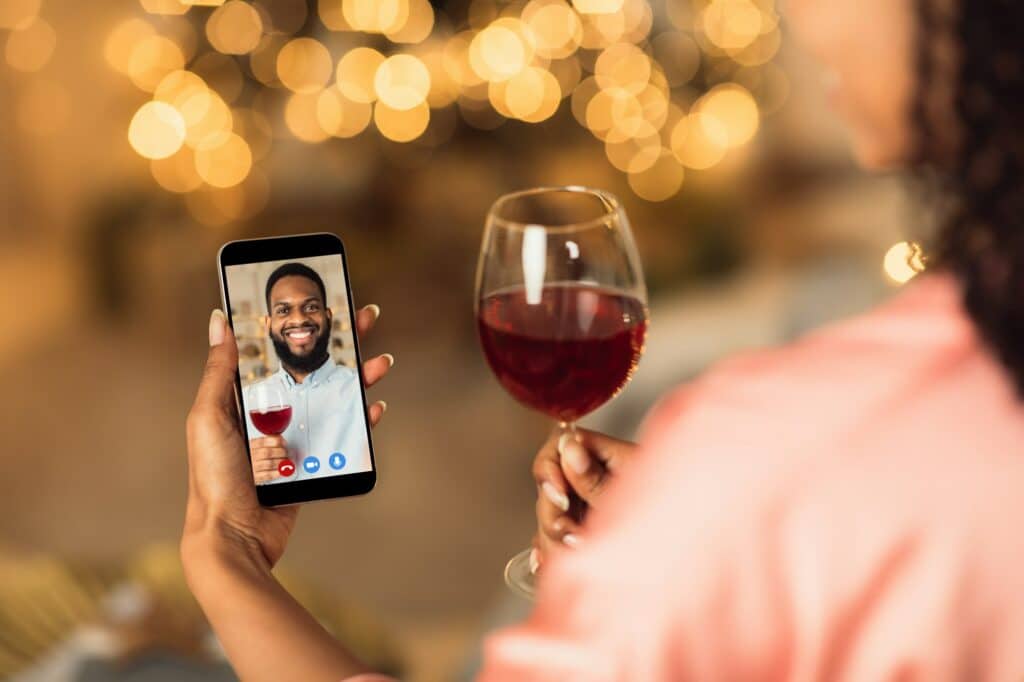 Black couple having online date on phone, drinking wine