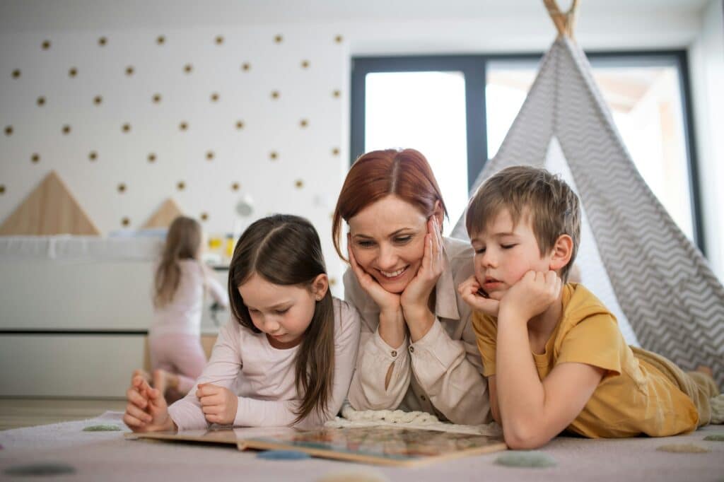 Mother with little children lying on floor and reading book at home