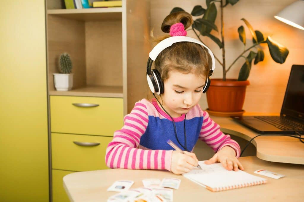 pre-school girl with headphones is engaged at home at the table studying