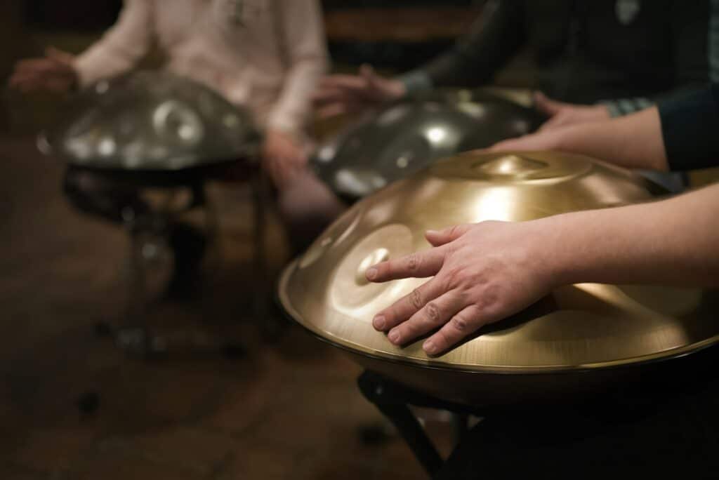 A musician's hand playing the handpan with other people.