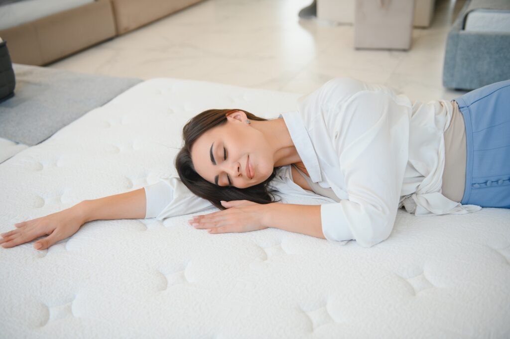 A woman in a white shirt in a mattress store. She examines the mattress she wants to buy