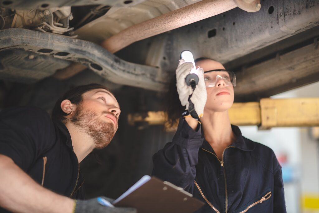 car mechanic standing under car in garage inspecting and doing maintenance work for car