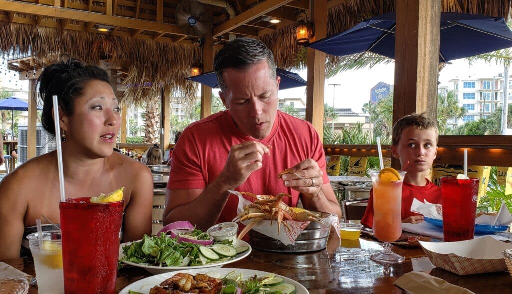 Generation X ethnic couple on vacation Eating crab legs with generation z nephew at beach.