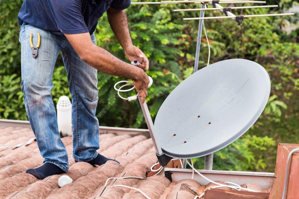 Worker installing satellite dish and antenna on roof top